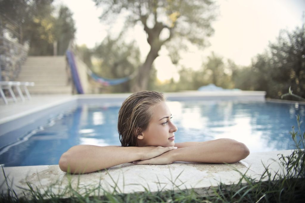 Side view of calm female with wet hair leaning on poolside while chilling in swimming pool during vacation and looking away